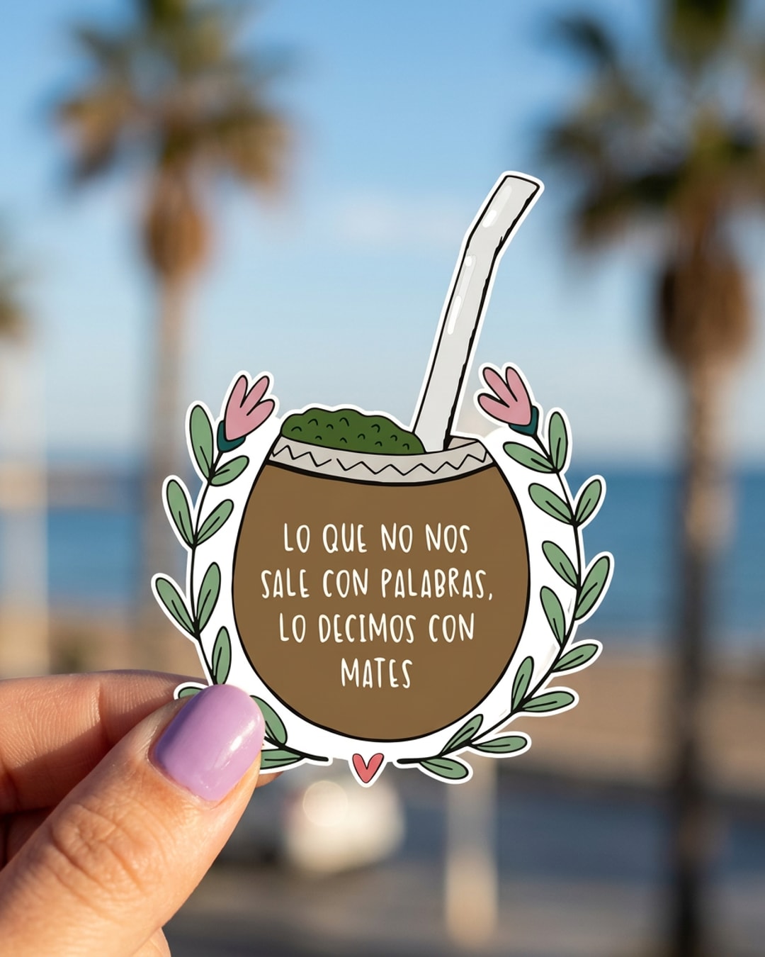 Pegatina Mate con frase Lo que no nos sale con palabras sostenida en la mano, a tamaño real