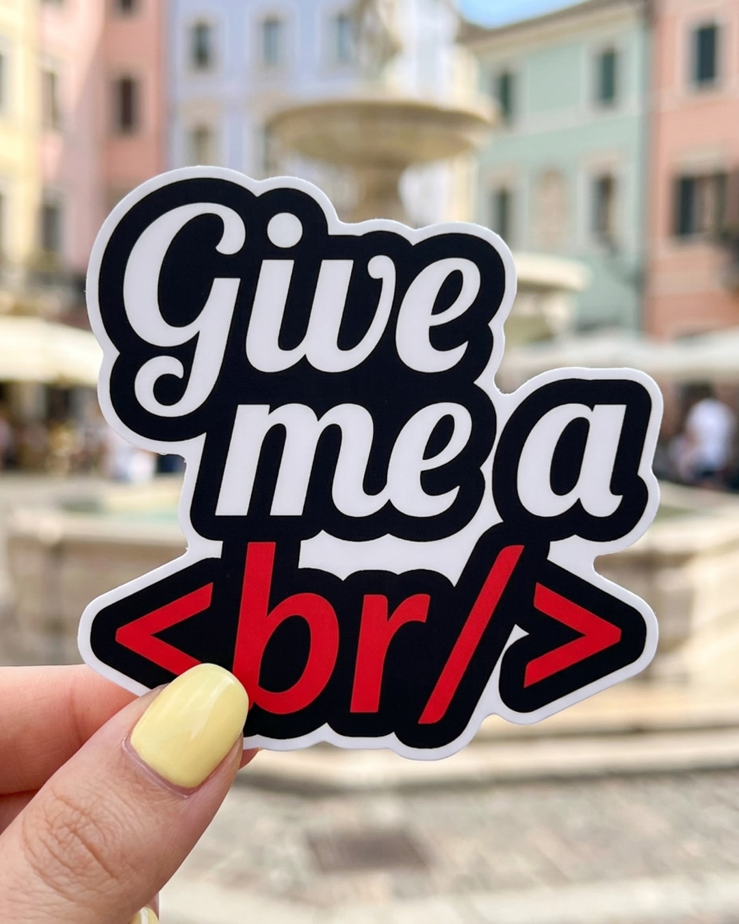 Pegatina Frase Give me a br para programadores sostenida en la mano, a tamaño real