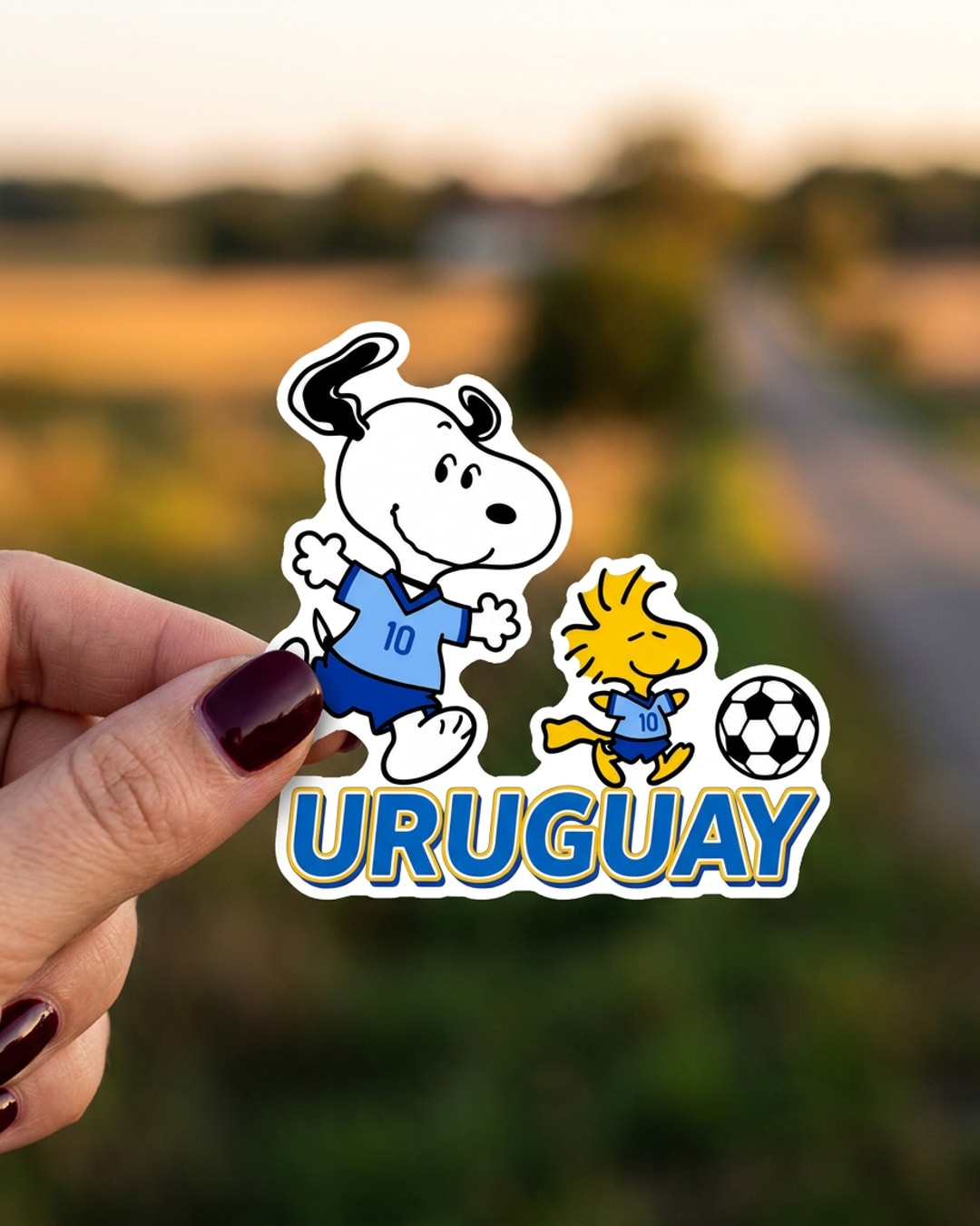 Pegatina Snoopy y Emilio de la selección de Uruguay sostenida en la mano, a tamaño real