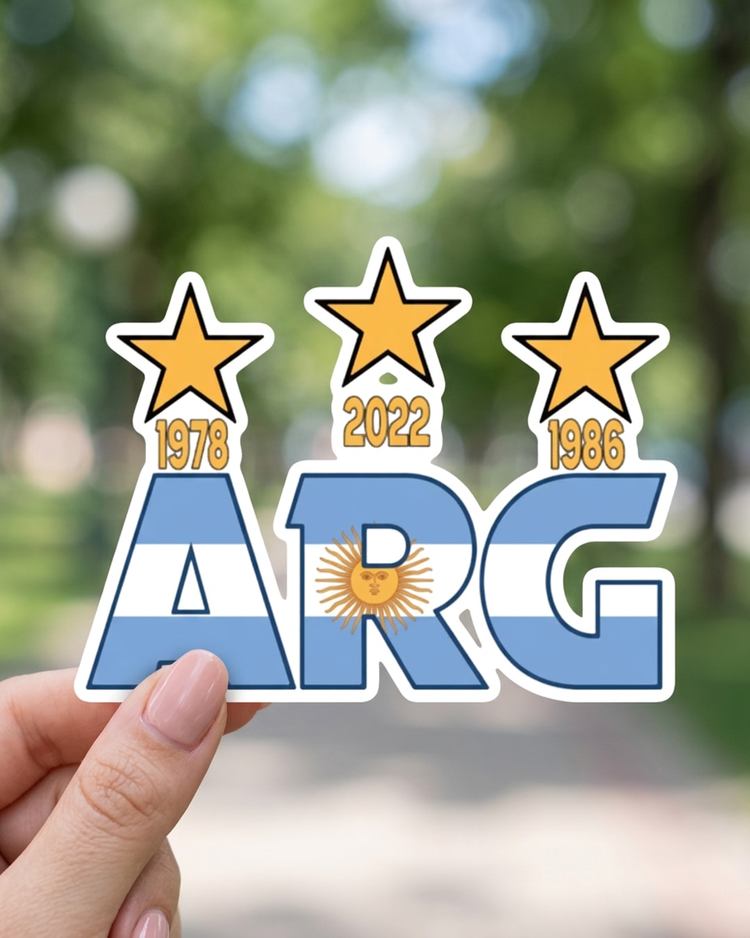 Pegatina ARG con Bandera de Argentina y Tres Estrellas sostenida en la mano, a tamaño real