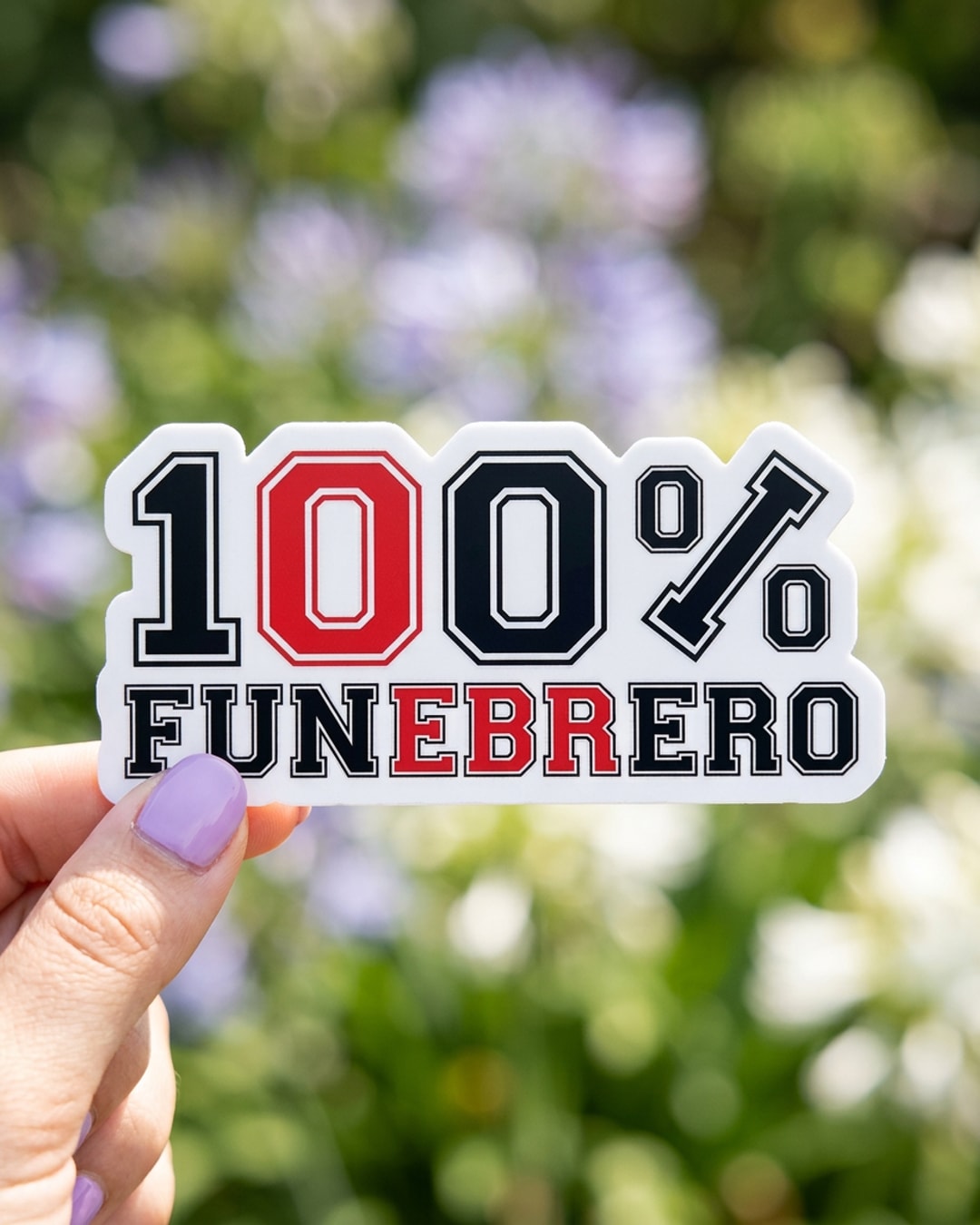 Pegatina 100% Funebrero sostenida en la mano, a tamaño real