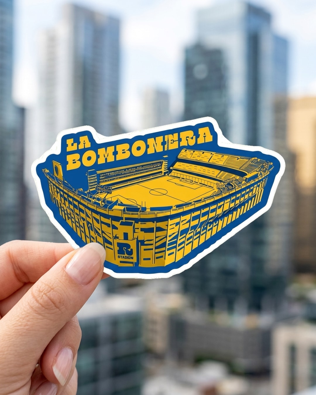 Pegatina Estadio La Bombonera azul y amarillo sostenida en la mano, a tamaño real